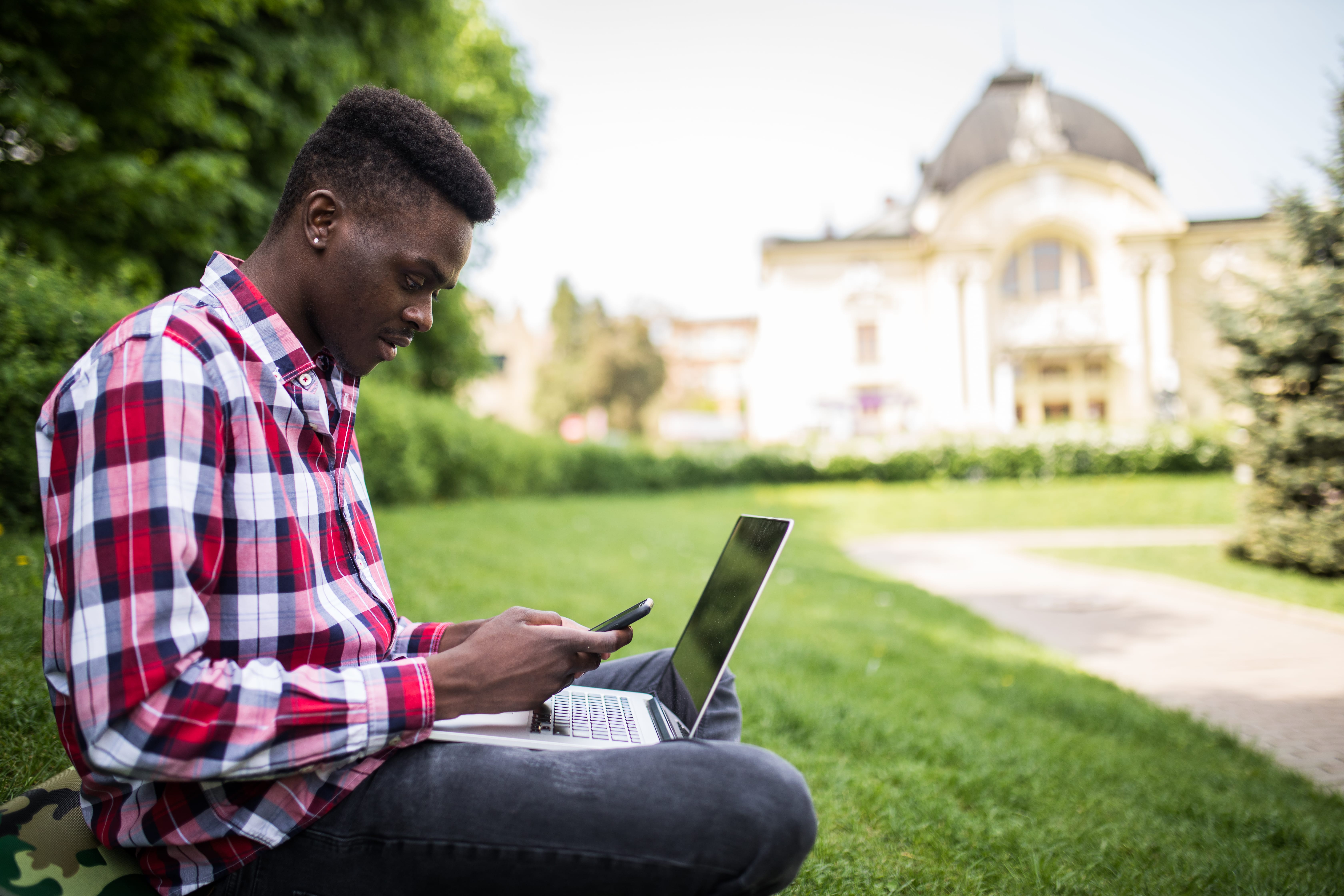 young attractive afro american businessman with laptop sitting grass talking cell phone park