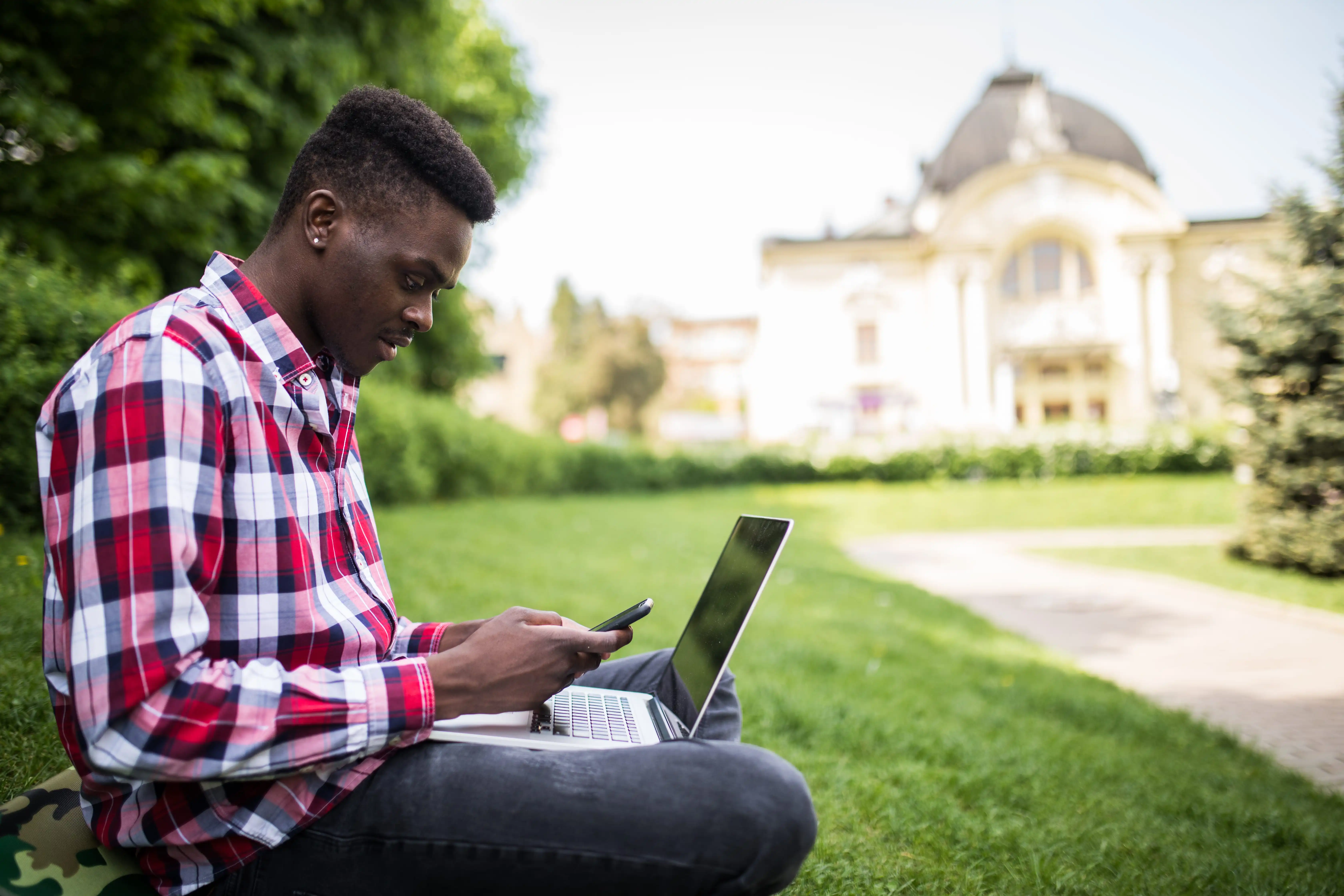 young attractive afro american businessman with laptop sitting grass talking cell phone park